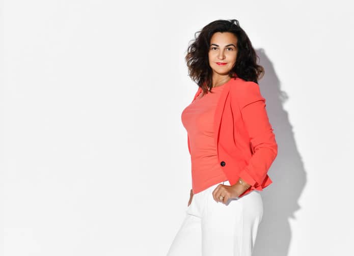 Middle-aged woman in orange jacket posing in front of a white background.