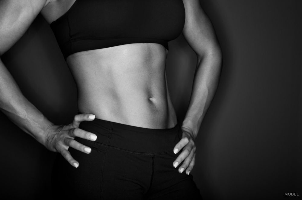 A black and white image showing a woman's midriff in black fitness clothes with hands on hips