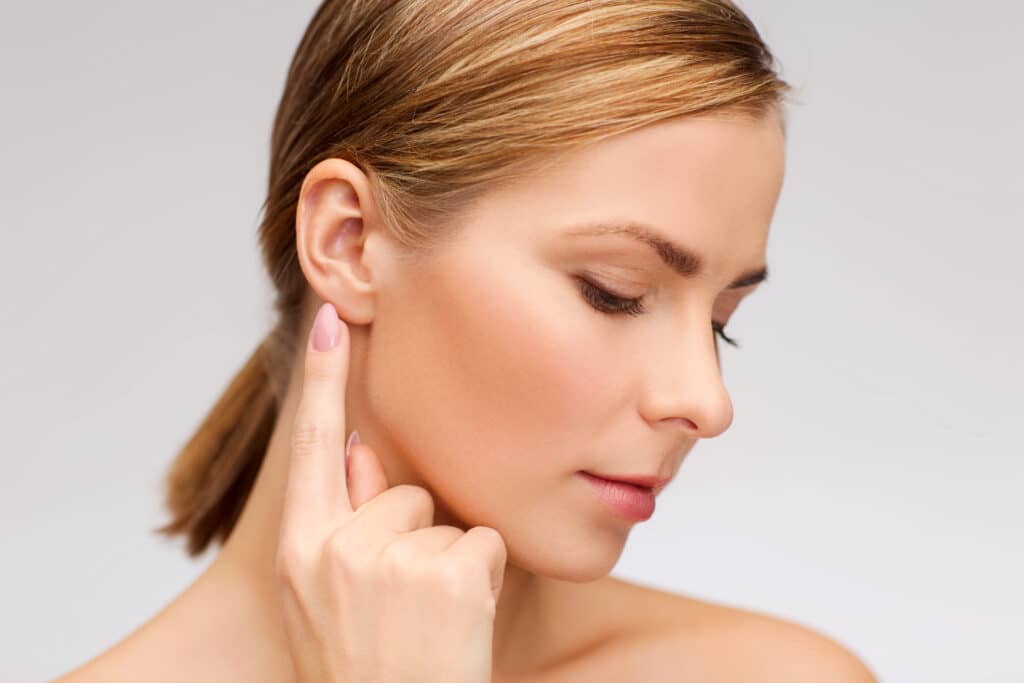 A woman looking down and pointing to her ear after ear pinning surgery